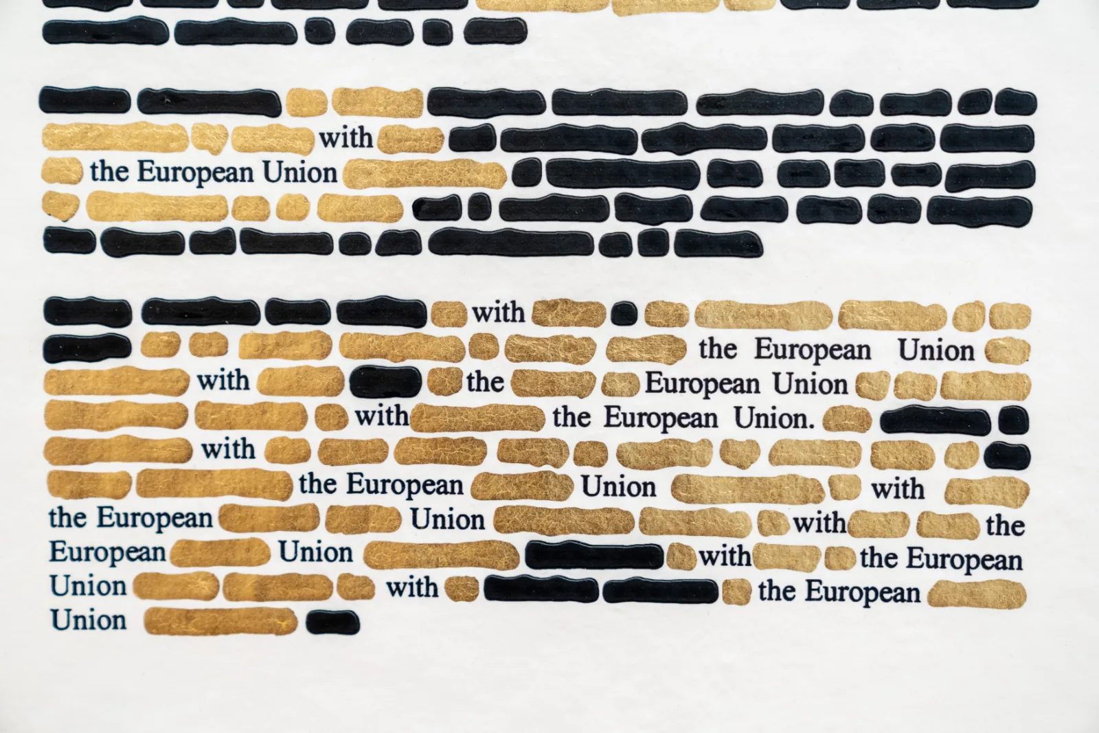 A detail of a sheet covered in black ink and gold leaf, with the words with the European Union surviving in black type and recurring line after line among the gilded bars