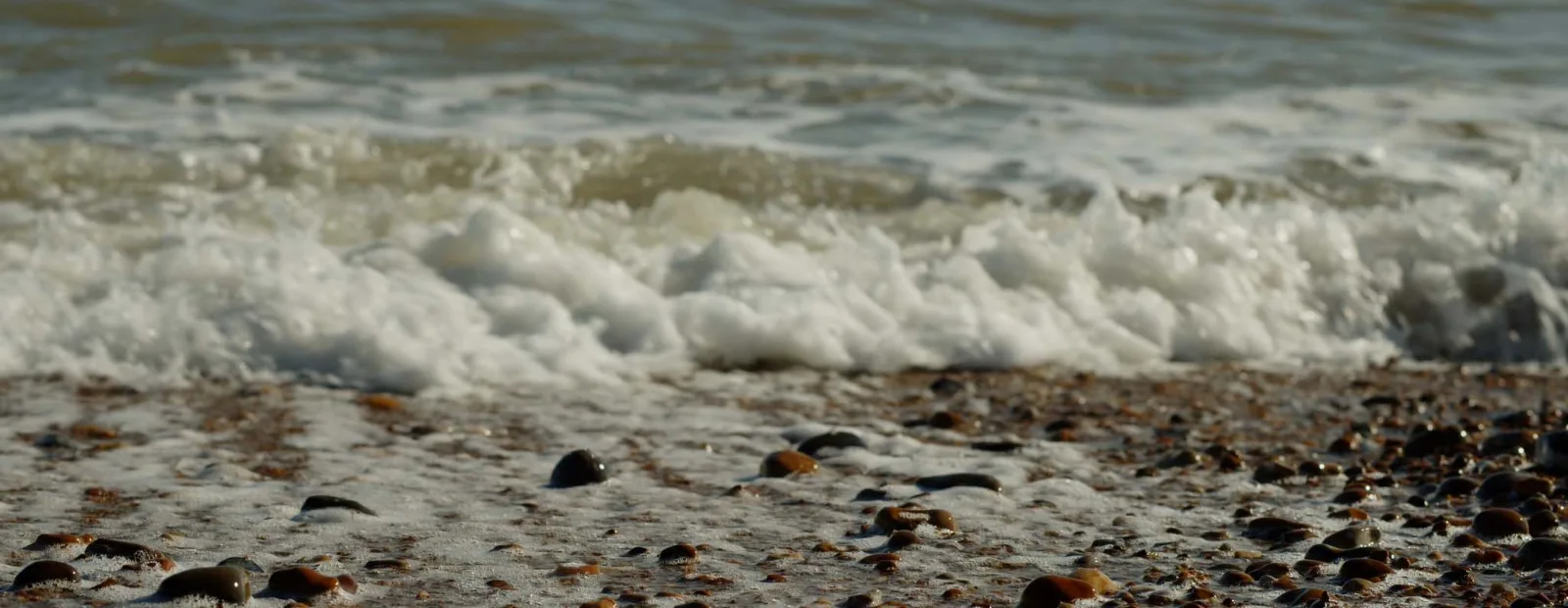 White foam of a breaking wave spreading over wet shingle, the stones shining brown and black