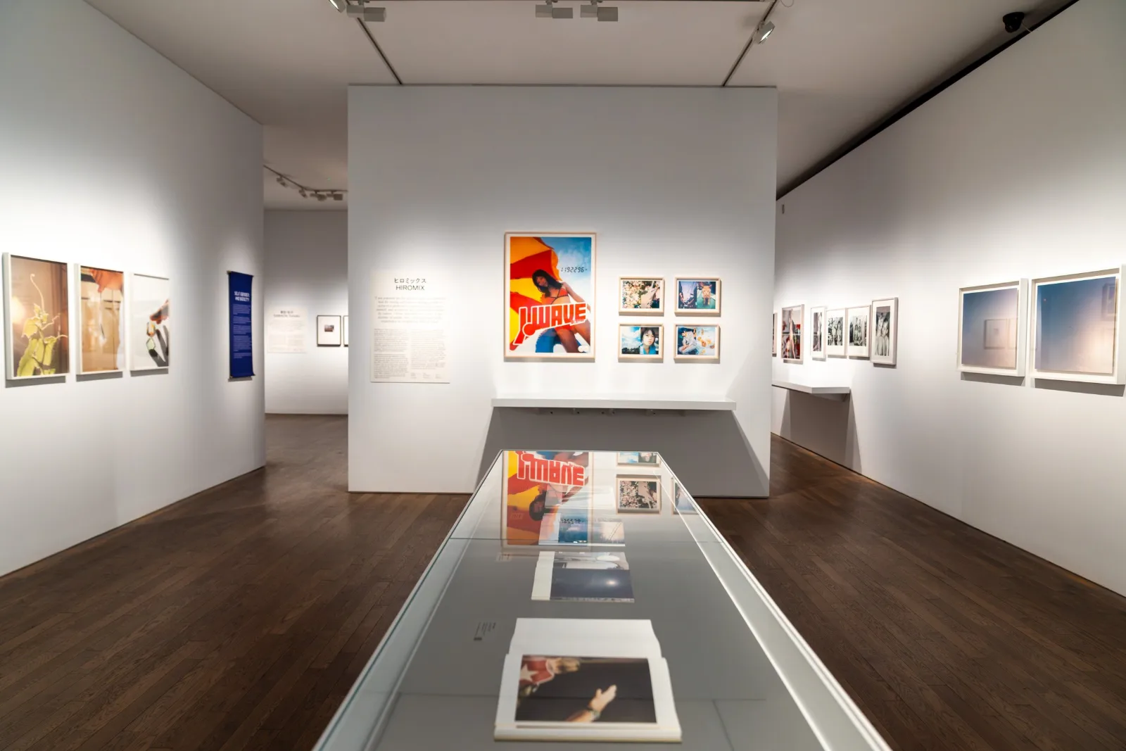Gallery view with framed photographs on white walls and a long glass vitrine of photobooks in the centre of the room