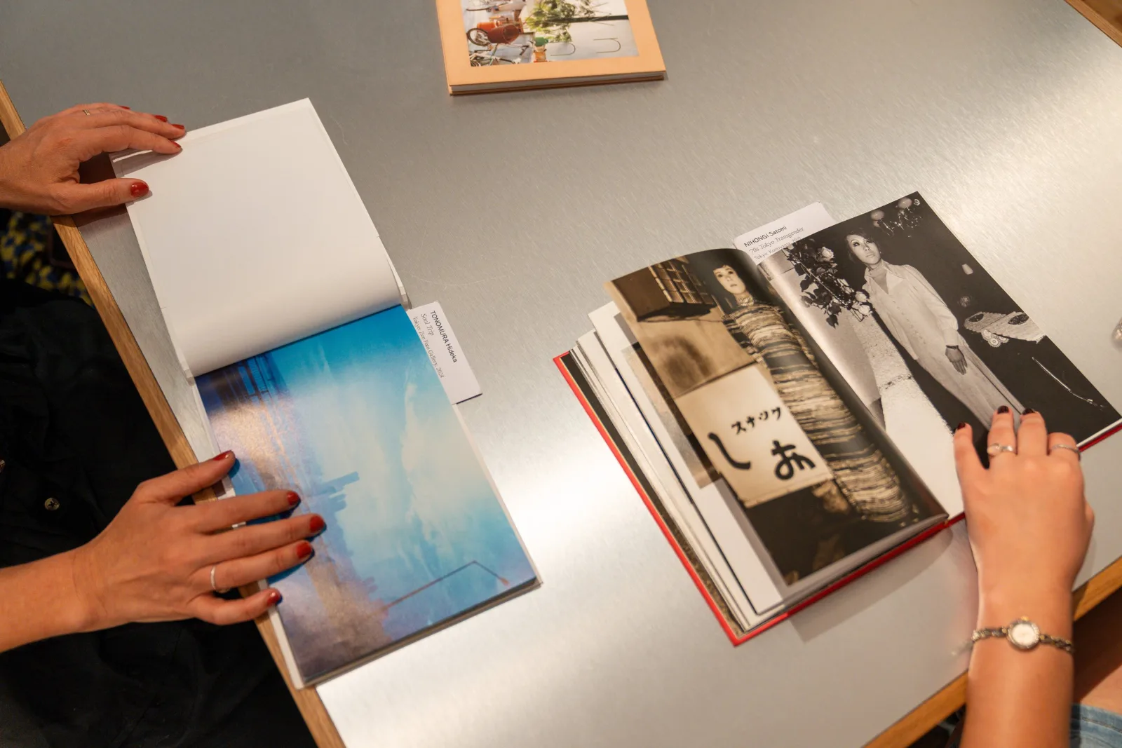 Hands leafing through open photobooks on a reading table