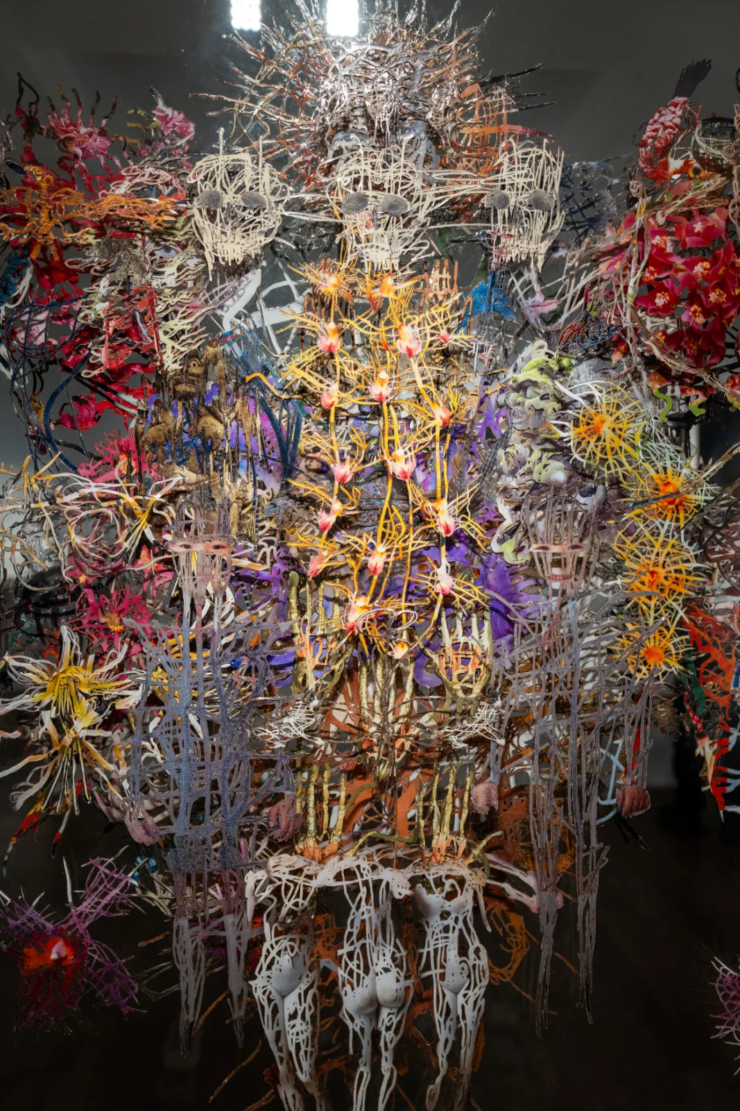 Close-up of a dense work of cut and layered images, with flowers, lace-like figures and small faces in bright colours against a dark background
