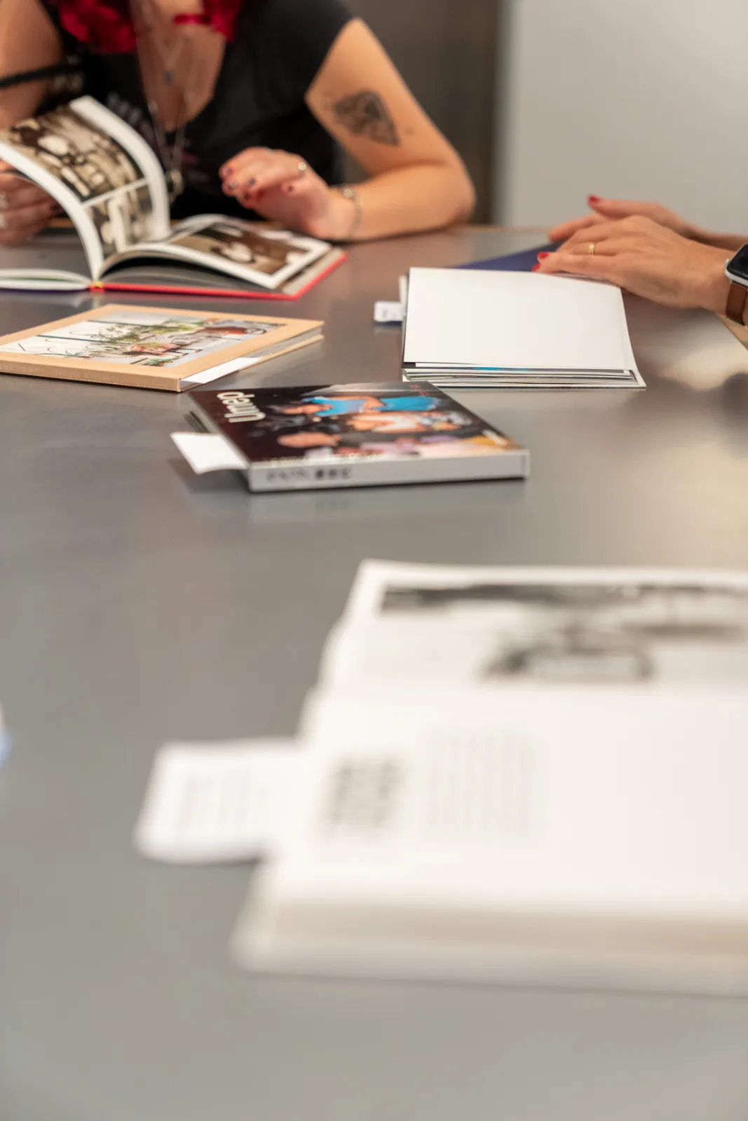 Photobooks spread on a grey reading table, with visitors turning the pages of an open book in the background