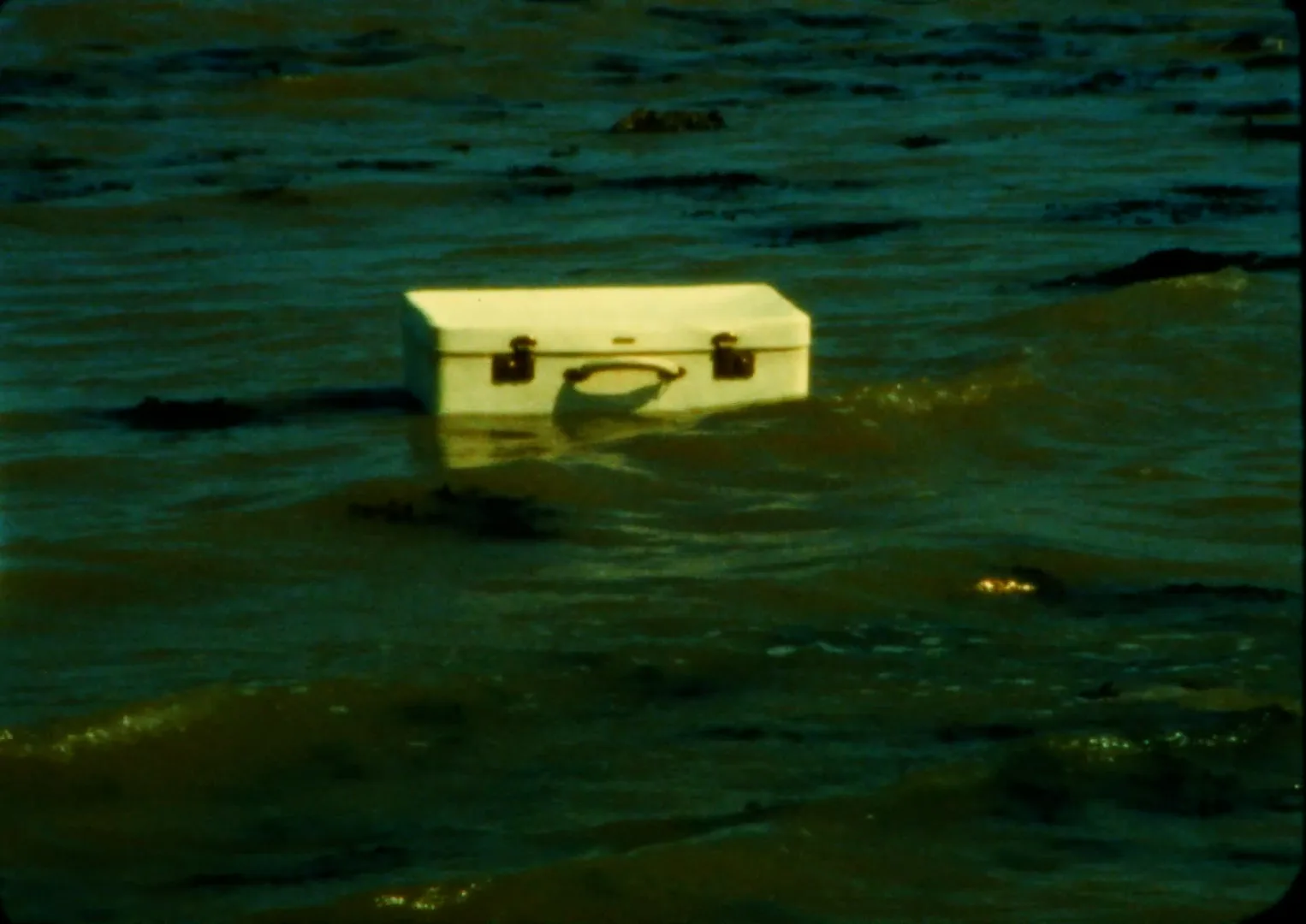 A closed wooden chest floating on the waves, carried by the sea towards the shore