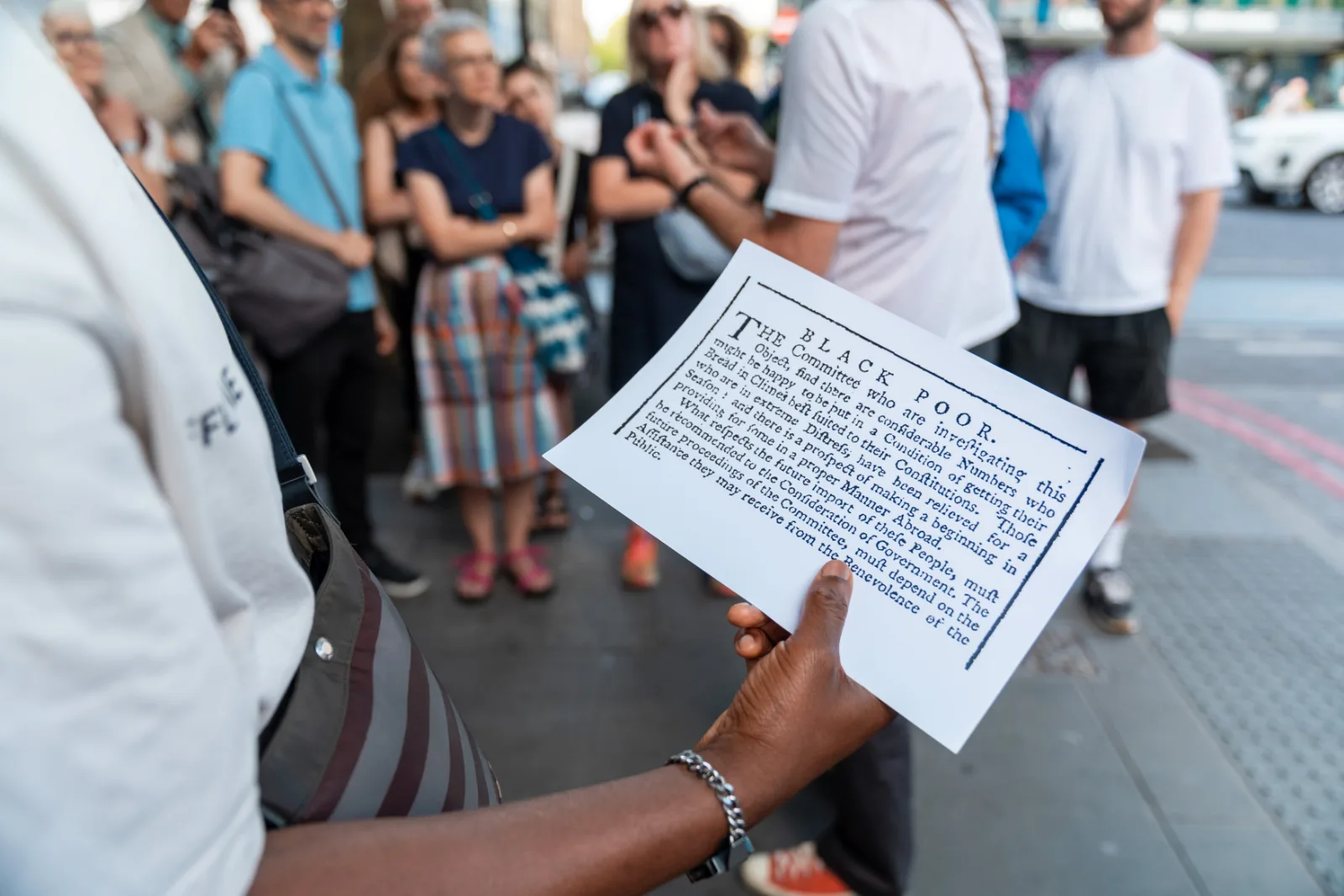 Hands holding up a printed archive document about the Black Poor, the walking group behind