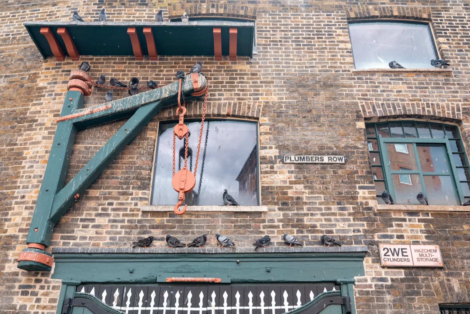 A brick facade on Plumbers Row with an old hoist above the windows and pigeons on the ledge