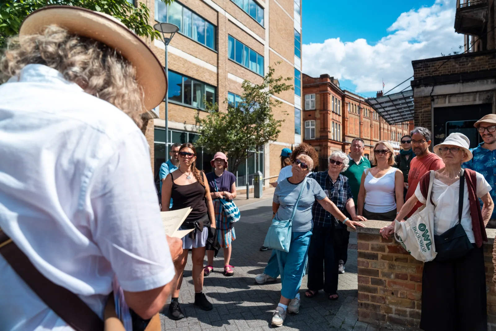 The walking group listening on the pavement, seen from behind the guide's shoulder