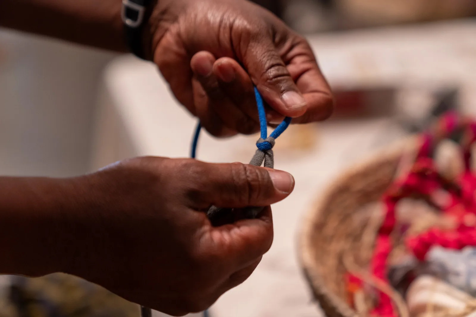 Hands knotting blue cord at the participatory table of The Ropery